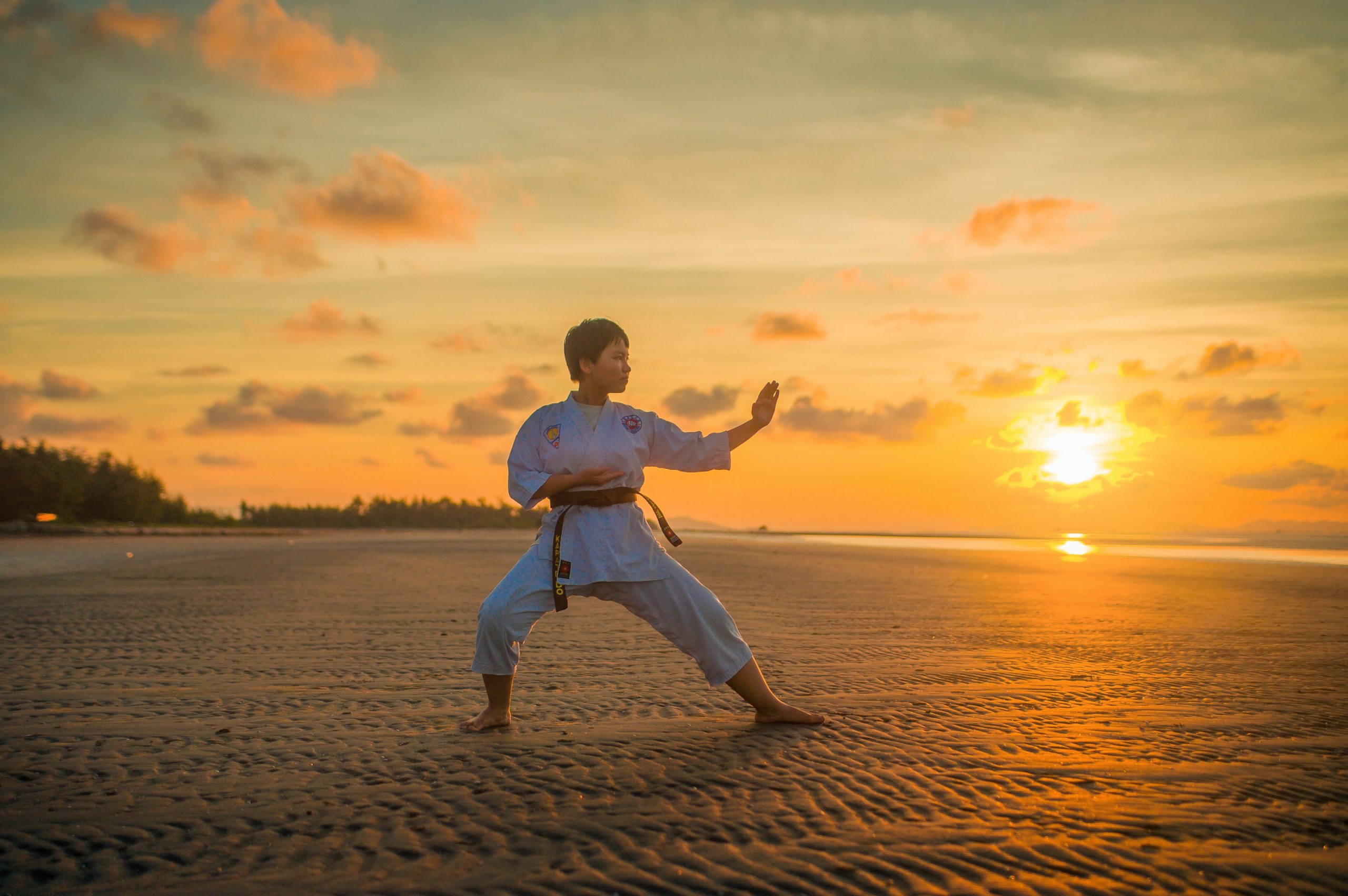 girl practicing martial arts on a beach with a sunset